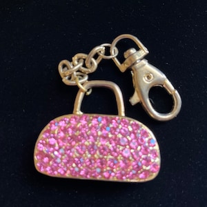 May include: A pink sparkly handbag keychain with a silver metal clasp.