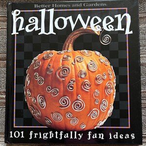 May include: A book titled "Halloween" by Better Homes and Gardens with a pumpkin decorated with silver swirls on the cover. The book title is in white text on a black background. The book cover also includes the text "101 frightfully fun ideas".