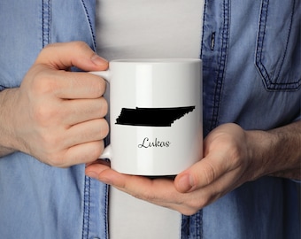 Puede incluir: Taza de cerámica blanca con un contorno negro del estado de Tennessee y el nombre "Lukas" impreso en cursiva negra.
