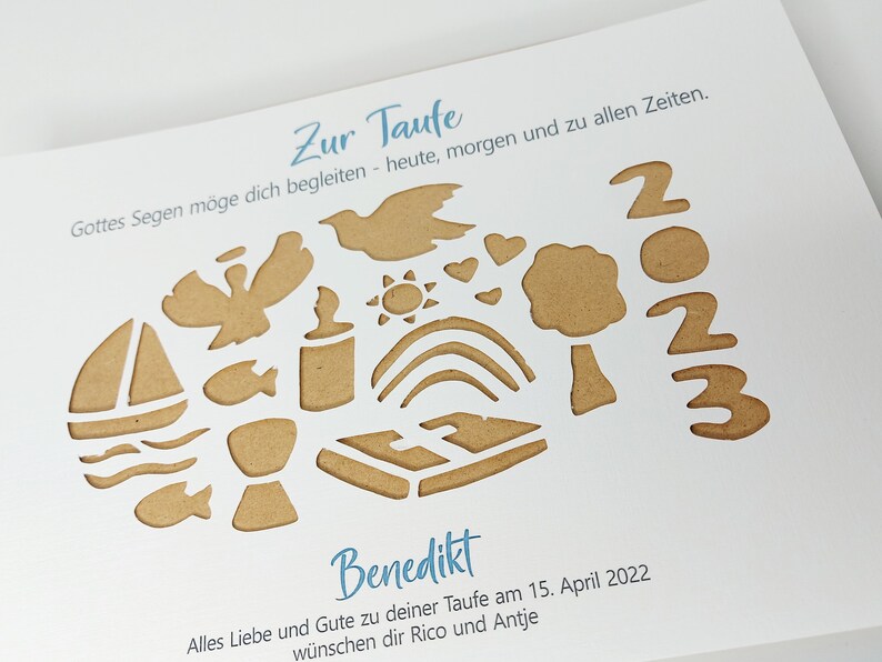 May include: A white card with a brown paper cut-out design. The design includes a dove, a sun, a rainbow, a tree, a chalice, a fish, a boat, and the numbers 2023. The text on the card reads "Zur Taufe", "Gottes Segen m&ouml;ge dich begleiten - heute, morgen und zu allen Zeiten.", "Benedikt", "Alles Liebe und Gute zu deiner Taufe am 15. April 2022", and "w&uuml;nschen dir Rico und Antje".