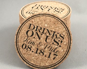May include: A stack of round cork coasters with black text that reads "DRINKS ON US!" and the names "Kim & Mike" with the date "08.18.17". The coasters have a dark border.