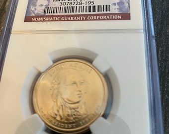 May include: A gold-colored coin in a plastic coin holder. The coin features a portrait of John Adams, the second president of the United States. The holder has a label that reads "Second President John Adams 2007P $1 Brilliant UNC. First Day of Issue 3078728-195 Numismatic Guaranty Corporation".