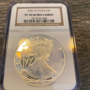 May include: A silver American Eagle coin graded PF 70 Ultra Cameo by the Numismatic Guaranty Corporation. The coin features Lady Liberty walking towards the sunrise with the inscription "In God We Trust" and the year "2006".