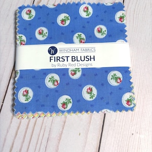 May include: A stack of blue fabric squares with a floral pattern. Each square features white circles with pink roses and green leaves. The fabric is labeled "FIRST BLUSH" by Ruby Red Designs, from Windham Fabrics.