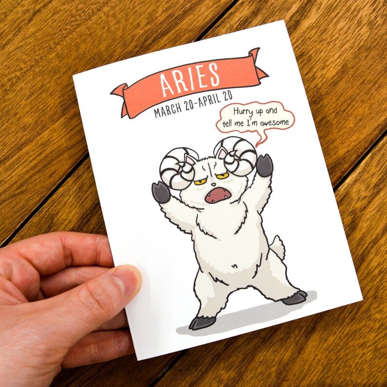 Pu&ograve; includere: Un biglietto bianco con un'illustrazione di un ariete bianco con un fumetto che dice "Hurry up and tell me I'm awesome". Il biglietto ha il testo "Aries March 20-April 20" su uno stendardo rosso.