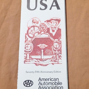 May include: A white brochure with the word "USA" in large, black letters at the top. The brochure features a red illustration of a vintage car and people. The text "Seventy-Fifth Anniversary Edition" is below the illustration, with the American Automobile Association logo and text below.