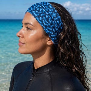 Puede incluir: Una cinta para el pelo ancha y elástica con un patrón abstracto de color azul oscuro y azul brillante que recuerda al coral. La cinta se coloca alrededor de la cabeza, sobre la frente y las orejas, y está hecha de un material liso y ligero.