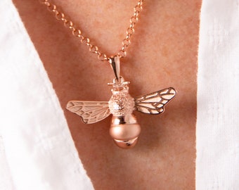 May include: A rose gold necklace with a bee pendant. The bee is detailed with textured wings and a round body.