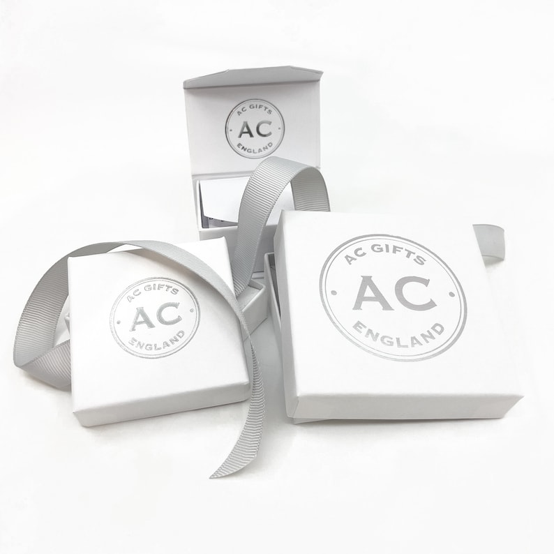 Op de afbeelding: Drie witte cadeaudozen met een zilveren logo met de tekst "AC Gifts England". De dozen zijn van verschillende grootte en zijn op elkaar gestapeld.