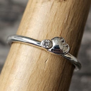 May include: A silver ring with a small heart-shaped design and a single clear stone.