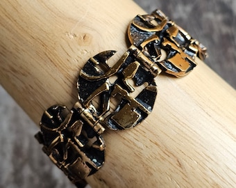 May include: A gold and black bracelet with a geometric design. The bracelet is made of metal and has a hinged clasp.