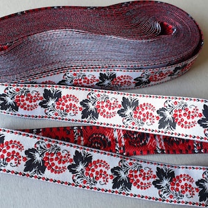 May include: A roll of decorative ribbon with a white base, featuring a repeating pattern of black leaves and red berries. A separate length of the ribbon is unrolled, showcasing the design. The ribbon's reverse side is red.