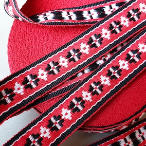 May include: Red, black, and white woven ribbon with a geometric pattern. The ribbon is rolled up and the ends are visible.