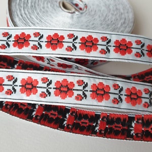 May include: White ribbon trim with a red and black floral pattern. The ribbon is folded and shows the pattern on both sides.