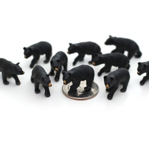 May include: A group of ten black bear figurines, each standing on a white surface. The bears are all facing different directions, and one bear is standing on a silver coin.