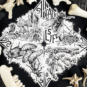 Puede incluir: Parche en blanco y negro con las palabras "IN DEATH IS LIFE" e ilustraciones de hongos, insectos y otros elementos naturales. El parche está rodeado de varios huesos de animales.