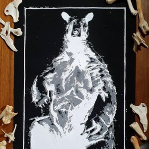 May include: Black and white print of a bear with its mouth open, printed on black fabric. The bear is in a sitting position with its paws visible.