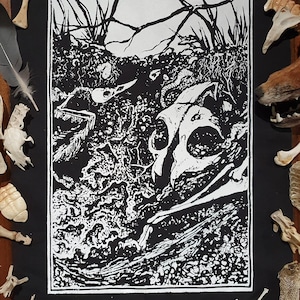 May include: Black and white print of a skull and bones on a black fabric patch. The print is a woodcut style and features a skull with a jawbone and other bones.