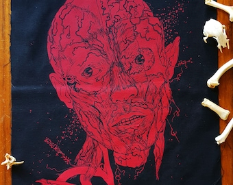 May include: Red anatomical illustration of a human face printed on black fabric. The face is detailed with muscles and veins. The fabric is surrounded by white bones.