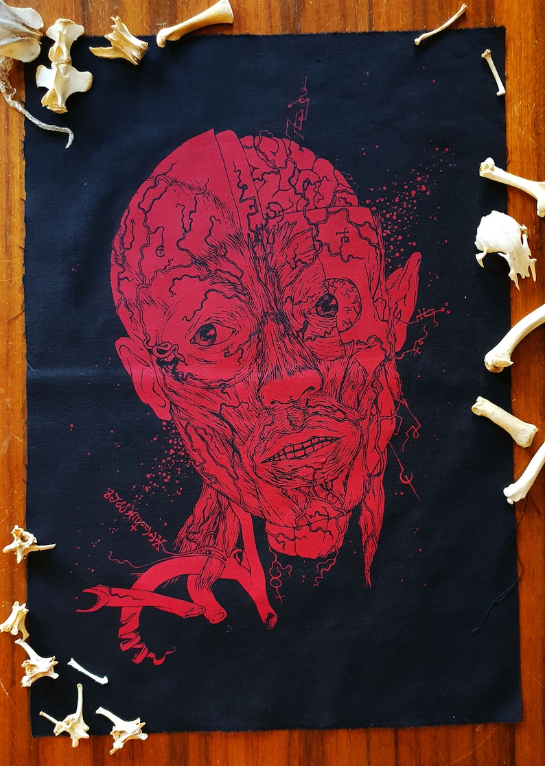 May include: Red anatomical illustration of a human face printed on black fabric. The face is detailed with muscles and veins. The fabric is surrounded by white bones.