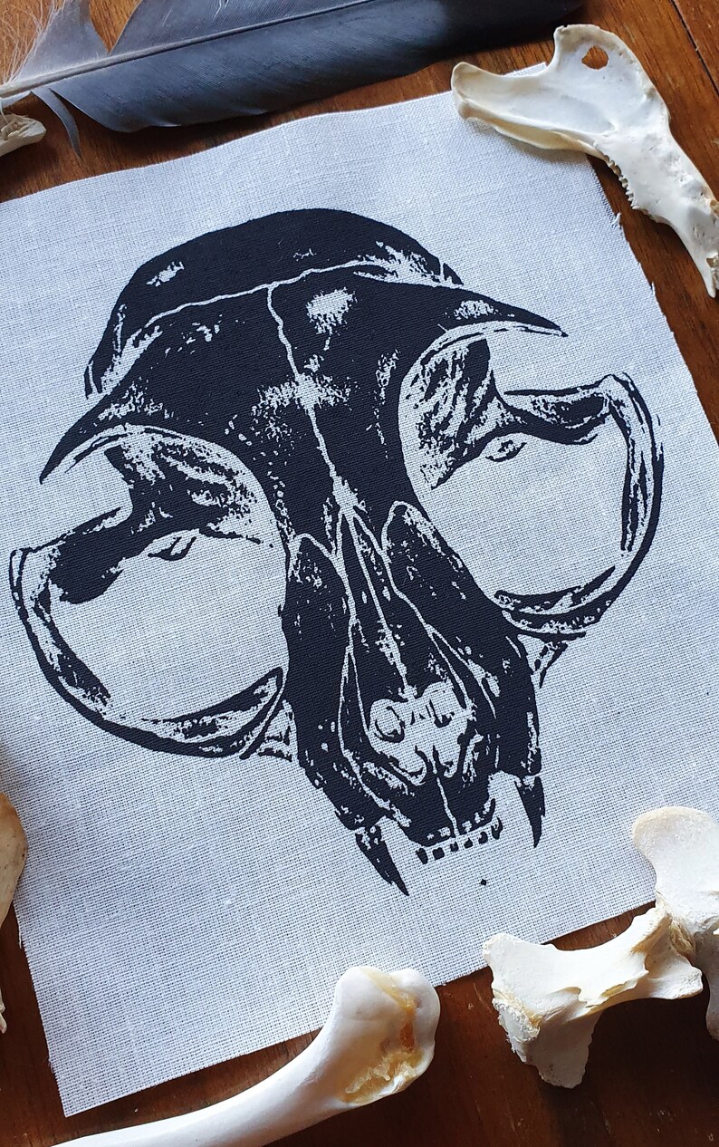 May include: Black and white printed image of an animal skull on a light gray fabric background. The skull is a close-up of the front of the skull, showing the teeth and eye sockets.