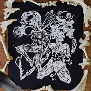 May include: A black fabric patch featuring a white screen-printed graphic of two surreal, humanoid figures with intricate, stippled textures. One figure has a large eye and flowing hair, while the other displays geometric shapes and organic forms.
