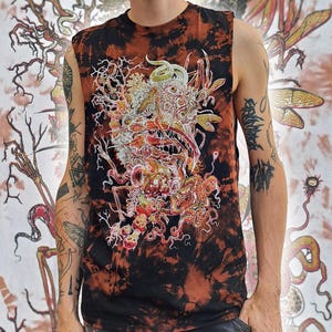 May include: A sleeveless shirt featuring a black and rust-coloured tie-dye pattern. The front displays a detailed, multi-coloured graphic illustration of a complex, surreal creature with multiple eyes, sharp teeth, and tentacle-like appendages.