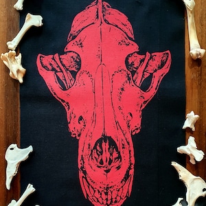 May include: Red printed skull of a dog on a black fabric patch. The skull is detailed and has a realistic look.