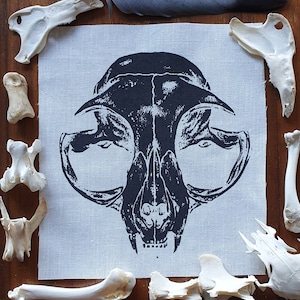 May include: Black and white printed fabric patch featuring a detailed illustration of a cat skull.