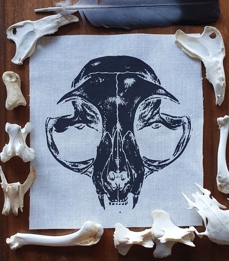 May include: Black and white printed fabric patch featuring a detailed illustration of a cat skull.
