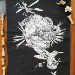 Puede incluir: Ilustración en blanco y negro de una serpiente envuelta alrededor de un cristal, un colibrí volando, una mantis religiosa y algunos insectos. La ilustración está sobre un fondo de tela negro.