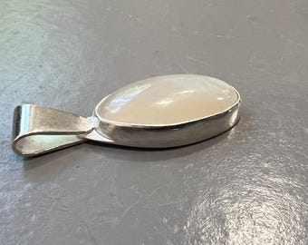 May include: A silver pendant with a pear-shaped, off-white gemstone. The gemstone is set in a polished silver bezel. The pendant has a simple, curved bail for a chain. The overall design is minimalist and elegant.