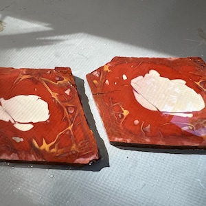 May include: Two irregularly shaped, reddish-brown wooden pieces with a white, cloud-like design in the center. The wood grain is visible, with gold and yellow veining throughout. The pieces are placed side by side.