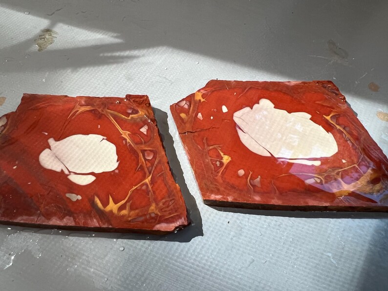 May include: Two irregularly shaped, reddish-brown wooden pieces with a white, cloud-like design in the center. The wood grain is visible, with gold and yellow veining throughout. The pieces are placed side by side.