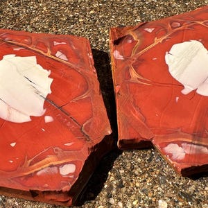 May include: Two rectangular, polished stone slabs. The slabs are primarily red with white and gold veining and a large white central area. The stone has a natural, organic appearance, suitable for decorative purposes.
