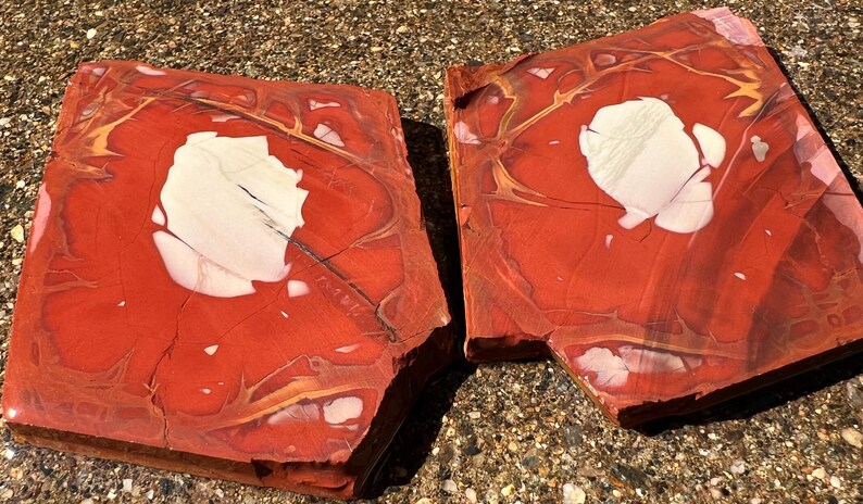 May include: Two rectangular, polished stone slabs. The slabs are primarily red with white and gold veining and a large white central area. The stone has a natural, organic appearance, suitable for decorative purposes.
