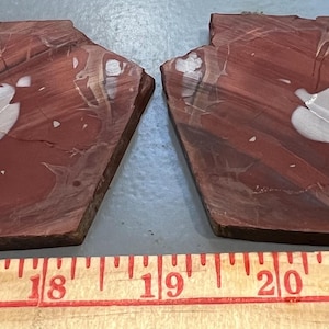 May include: Two reddish-brown, irregularly shaped stone slabs with a white, cloud-like pattern in the center. The slabs are placed side by side, with a wooden ruler below, showing measurements from 15 to 22 inches.