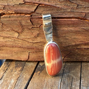 May include: A silver pendant with a red and white striped stone. The stone is oval shaped and has a smooth, polished finish.