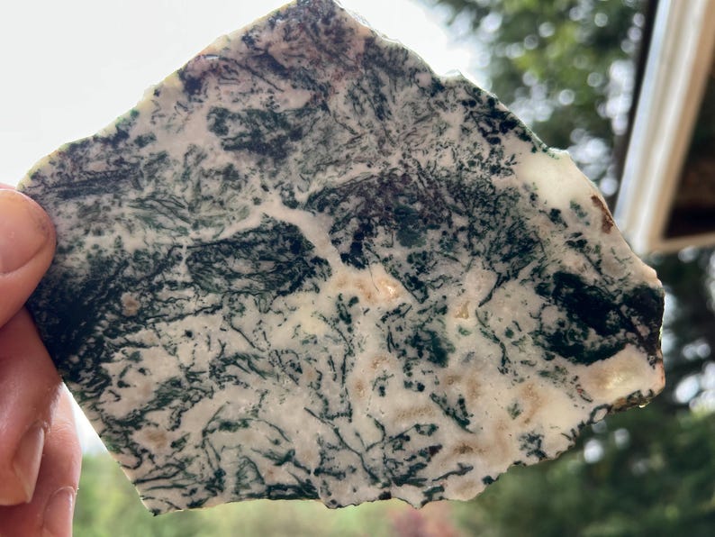May include: A natural stone slab with a unique pattern of green, white, and tan colors. The stone has a rough, irregular shape and a polished surface. The intricate veining creates a natural, artistic design. This decorative stone is ideal for home decor.