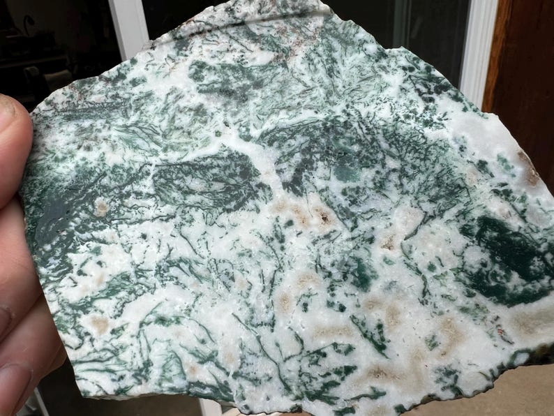 May include: A natural stone slab with a unique pattern of white, green, and brown hues. The stone's surface features intricate, vein-like patterns, creating a textured appearance. The irregular shape and color variations suggest a raw, organic origin.