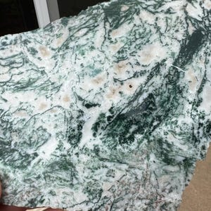 May include: A natural stone slab with a striking pattern of green, white, and tan hues. The stone's surface features intricate veining and a unique, organic design. This decorative stone is ideal for home decor and craft projects.