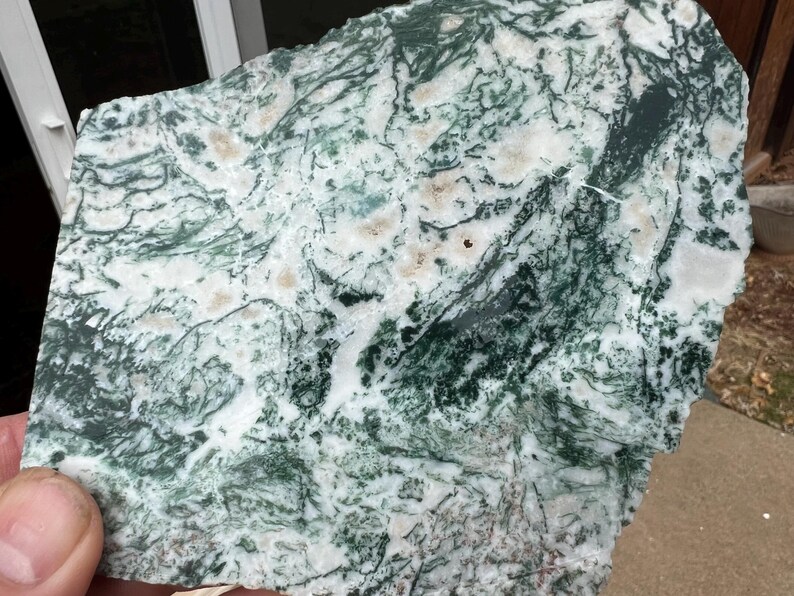 May include: A natural stone slab with a striking pattern of green, white, and tan hues. The stone's surface features intricate veining and a unique, organic design. This decorative stone is ideal for home decor and craft projects.