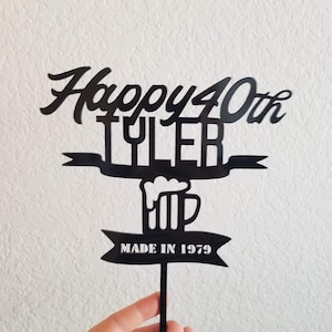 Op de afbeelding: Zwarte acryl taarttopper met de tekst "Happy 40th Tyler" en een bierpul-afbeelding met de tekst "Made in 1979".