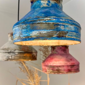 May include: Three hanging pendant lights with a rustic, distressed finish. The shades are painted in shades of blue, white, and red. The lights are suspended from black cords, creating a unique and artistic lighting fixture.