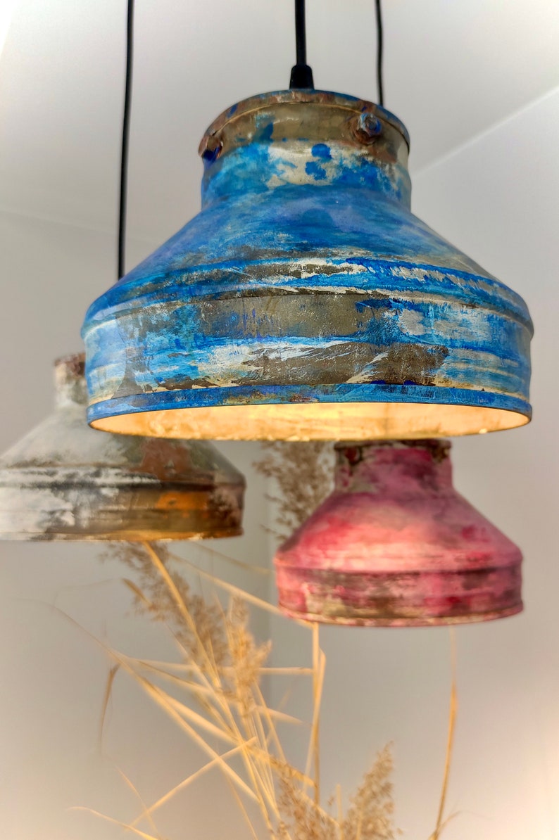 May include: Three hanging pendant lights with a rustic, distressed finish. The shades are painted in shades of blue, white, and red. The lights are suspended from black cords, creating a unique and artistic lighting fixture.