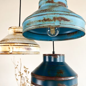 May include: Three pendant lights with distressed metal shades in blue, teal, and white. The shades have a rustic, vintage look with visible rust and wear.