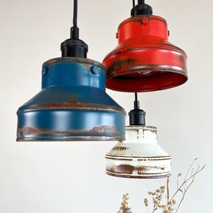 May include: Three pendant lights with a rustic, industrial style. The lights are made of metal and have a distressed finish. The shades are red, blue, and white.