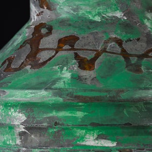 May include: Close-up of a green and brown decorative object with a textured surface. The object has a metallic appearance with a distressed finish, featuring a layered design and a dark background.