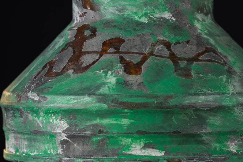 May include: Close-up of a green and brown decorative object with a textured surface. The object has a metallic appearance with a distressed finish, featuring a layered design and a dark background.