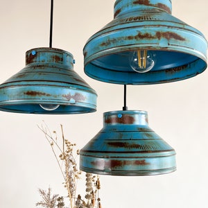 May include: Three blue metal pendant lights with a distressed finish. The lights have a wide, rounded shape and are hanging from black cords.